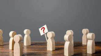 Wooden peg people standing around, with one holding a protest sign with a red question mark on it. | Andrii Yalanskyi | Dreamstime.com