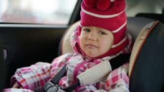 A sad little girl sits in a car seat in the back, bundled up. | Reana | Dreamstime.com