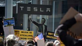 A protest outside a Tesla dealership in New York City, with a cardboard cutout of CEO Elon Musk. | Cpenler | Dreamstime.com
